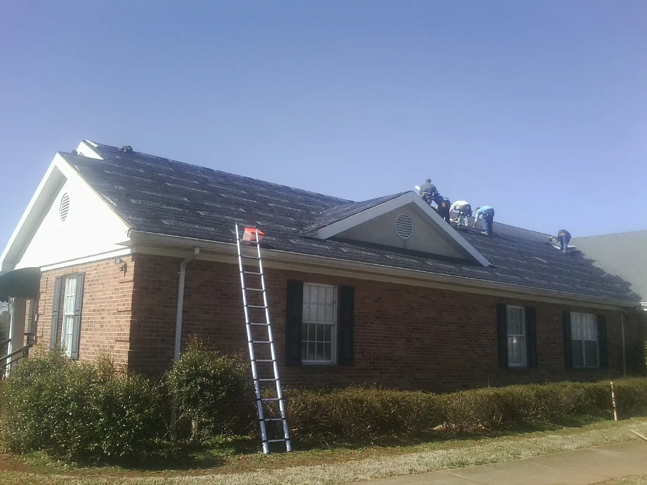 Crew tearing shingles off a brick ranch roof with a ladder set — Emergency Roof Repair work by our crew in Buckingham
