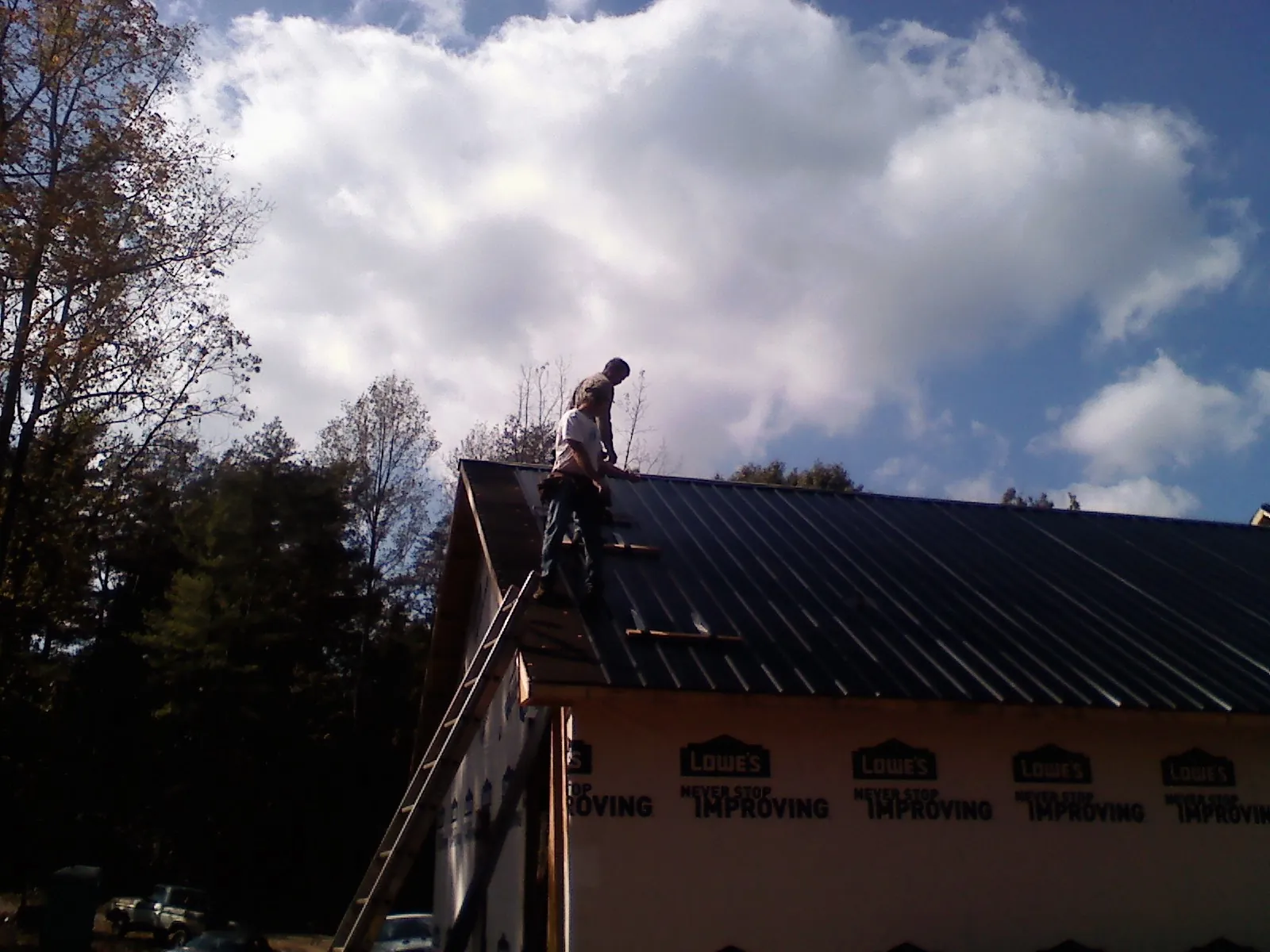 Roofer fastening dark metal panels high against a cloudy sky, from a Roof Inspection job in Buckingham